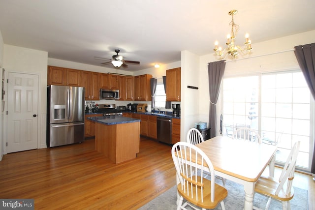 kitchen with a kitchen island, appliances with stainless steel finishes, ceiling fan with notable chandelier, pendant lighting, and light hardwood / wood-style flooring