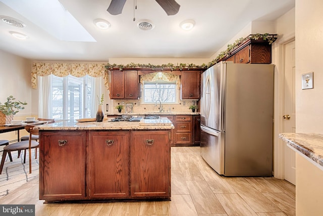 kitchen featuring sink, stainless steel refrigerator, a skylight, light stone counters, and a kitchen island