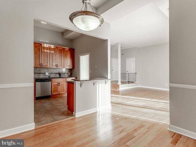 kitchen featuring a breakfast bar, dishwasher, sink, decorative backsplash, and light hardwood / wood-style floors