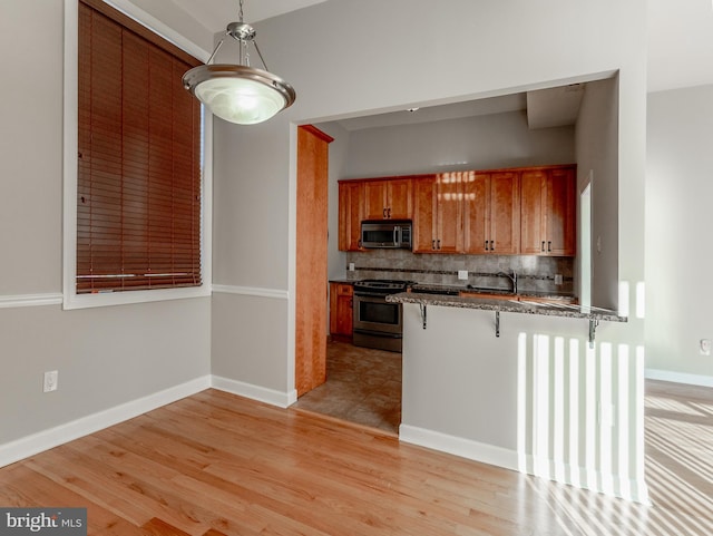 kitchen with appliances with stainless steel finishes, a breakfast bar, decorative light fixtures, decorative backsplash, and kitchen peninsula