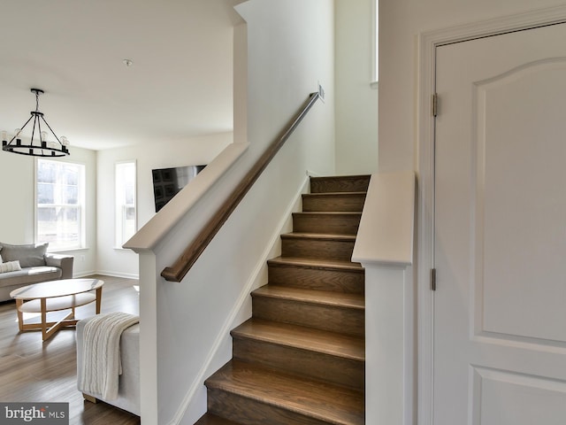 stairway featuring an inviting chandelier, wood finished floors, and baseboards