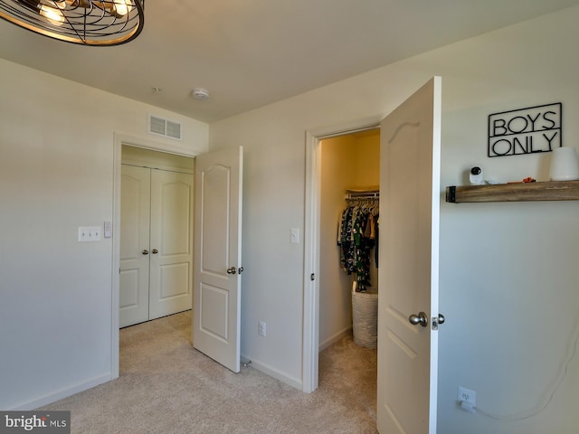 bedroom with a walk in closet, baseboards, visible vents, and light carpet