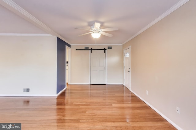 spare room featuring ornamental molding, a barn door, ceiling fan, and light wood-type flooring