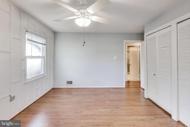 unfurnished bedroom with two closets, light hardwood / wood-style flooring, and ceiling fan