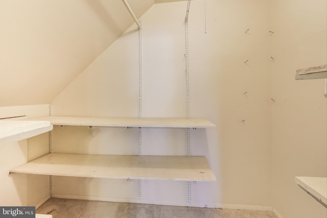 walk in closet with light colored carpet and lofted ceiling