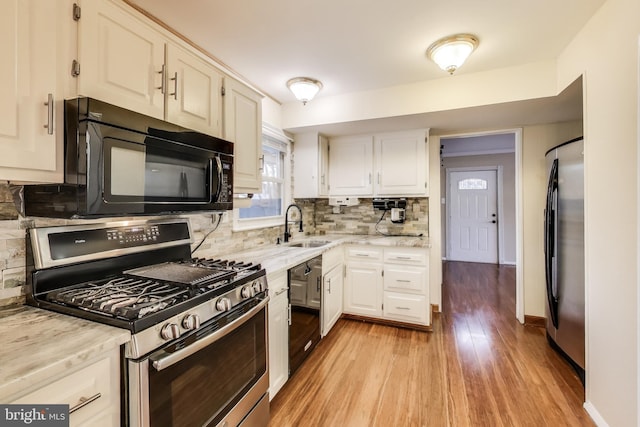 kitchen featuring sink, light hardwood / wood-style flooring, backsplash, black appliances, and white cabinets