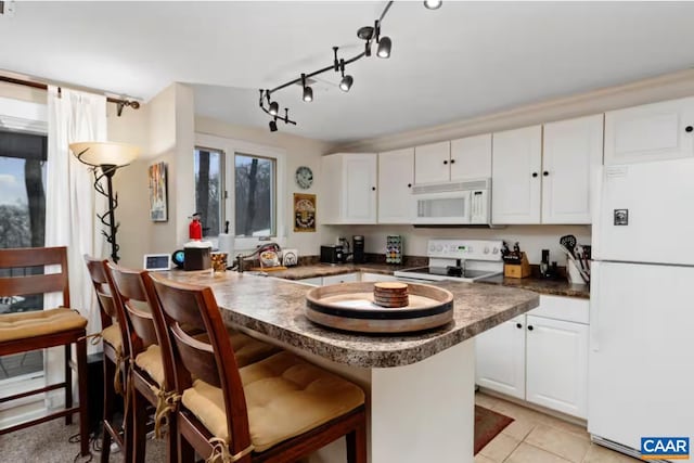 kitchen featuring light tile patterned floors, white appliances, a breakfast bar area, white cabinetry, and kitchen peninsula