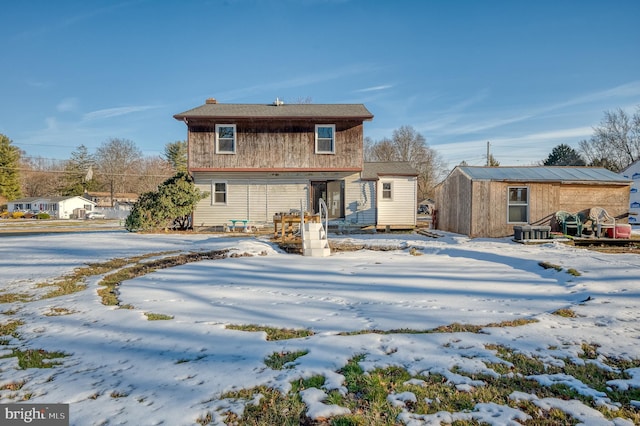 snow covered rear of property featuring cooling unit and a storage shed