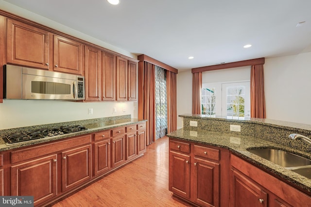 kitchen with dark stone countertops, sink, light hardwood / wood-style flooring, and appliances with stainless steel finishes