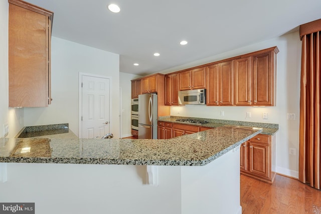 kitchen with a breakfast bar area, light stone counters, kitchen peninsula, stainless steel appliances, and light wood-type flooring