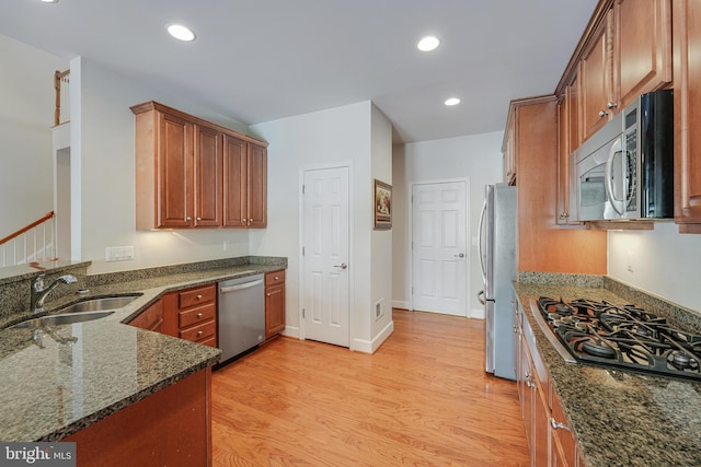 kitchen featuring stainless steel appliances, sink, dark stone countertops, and light hardwood / wood-style floors