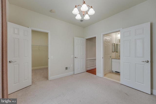 unfurnished bedroom with connected bathroom, a spacious closet, light carpet, an inviting chandelier, and a closet