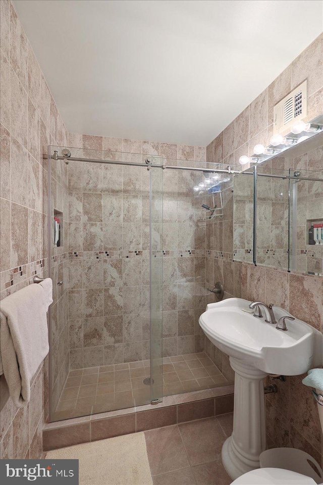 bathroom featuring toilet, tile walls, tile patterned floors, and a shower with shower door