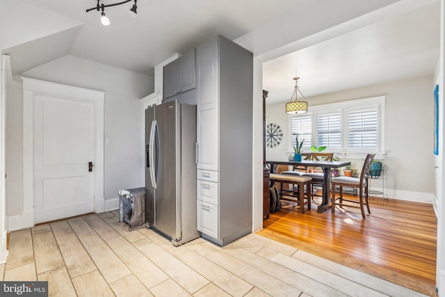 kitchen featuring vaulted ceiling, decorative light fixtures, stainless steel fridge, and light hardwood / wood-style flooring