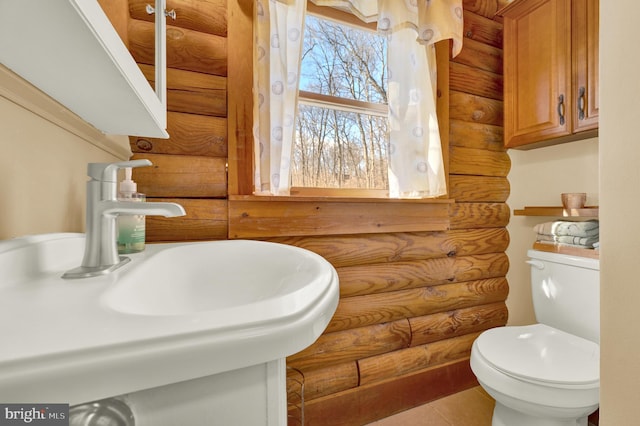 bathroom with toilet, a sink, and log walls