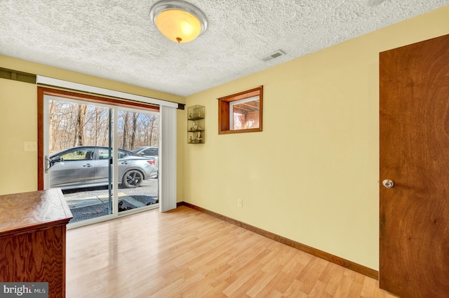 spare room with light wood-style flooring, visible vents, baseboards, and a textured ceiling