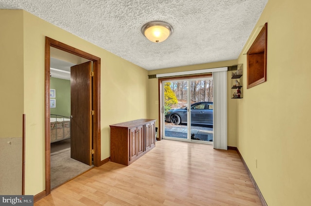 hall with a textured ceiling, baseboards, and light wood-style floors