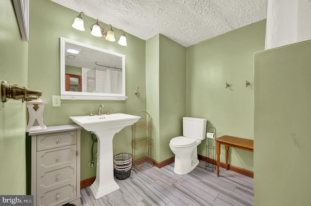 full bath featuring toilet, baseboards, a textured ceiling, and wood finished floors