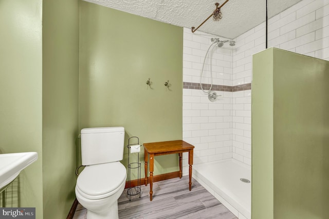 full bath featuring a textured ceiling, a tile shower, toilet, and baseboards