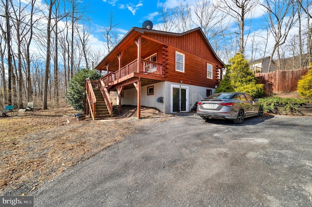 view of front facade featuring stairway, fence, log siding, driveway, and a wooden deck