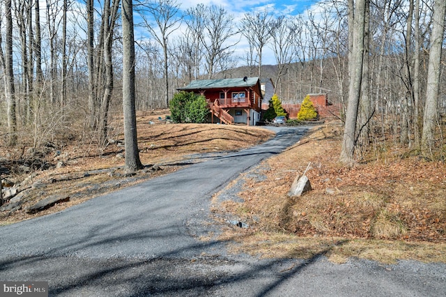 view of front of house featuring aphalt driveway, stairway, and a forest view