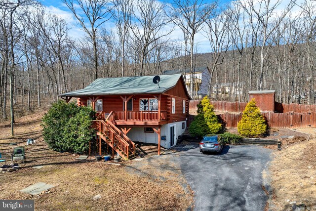 view of front facade featuring fence, driveway, stairway, log exterior, and a view of trees