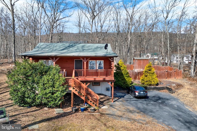 rear view of house featuring driveway, fence, stairway, and a wooded view