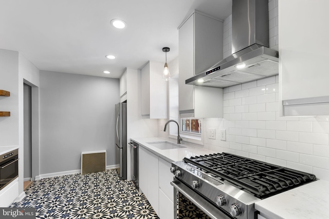 kitchen with decorative light fixtures, white cabinetry, sink, stainless steel appliances, and wall chimney range hood