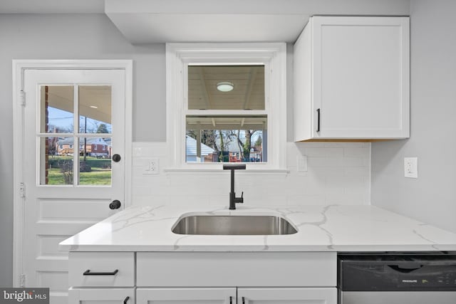 kitchen featuring white cabinets, sink, dishwashing machine, and light stone counters