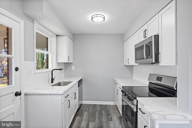 kitchen with sink, appliances with stainless steel finishes, white cabinetry, wood-type flooring, and light stone countertops