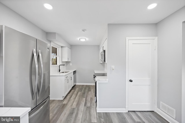 kitchen with sink, light hardwood / wood-style floors, white cabinets, and appliances with stainless steel finishes