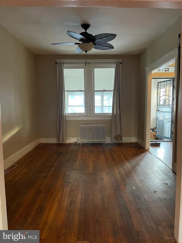 spare room with dark wood-type flooring, ceiling fan, and radiator