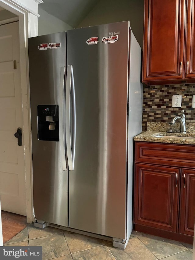 kitchen featuring backsplash, light stone countertops, sink, and stainless steel refrigerator with ice dispenser