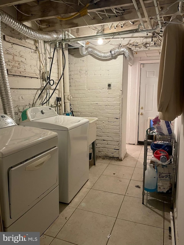 clothes washing area with brick wall, washer and dryer, and light tile patterned floors