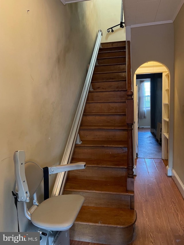 staircase with wood-type flooring and ornamental molding