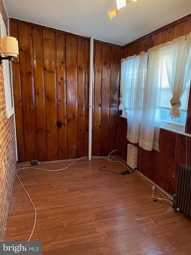 unfurnished room featuring radiator, hardwood / wood-style floors, and wood walls