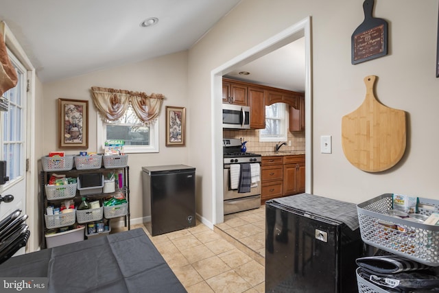 kitchen with lofted ceiling, light tile patterned floors, sink, appliances with stainless steel finishes, and backsplash