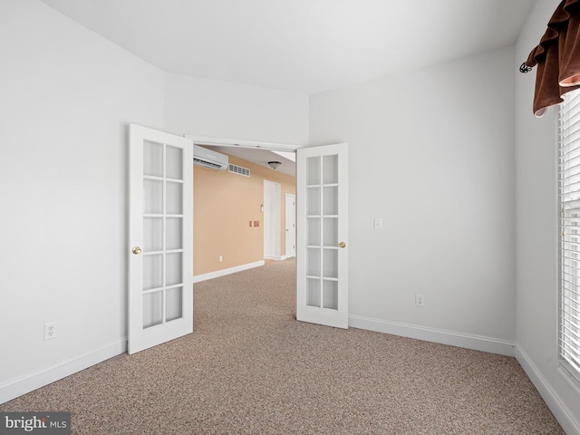 carpeted empty room featuring a wall unit AC, baseboards, visible vents, and french doors