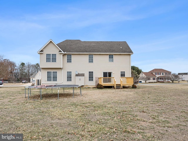 rear view of house with a trampoline, a lawn, a deck, and a shingled roof