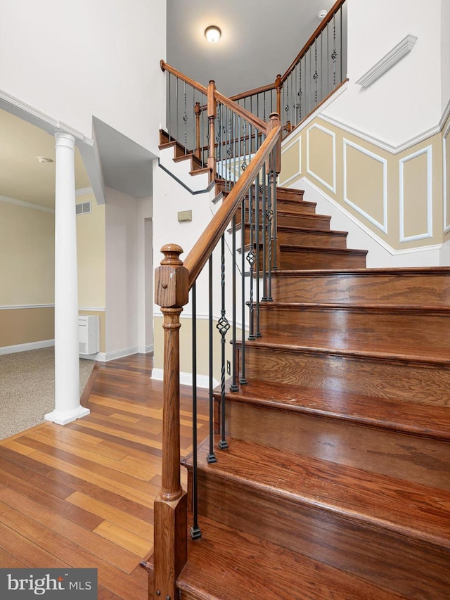 stairway featuring wood finished floors, visible vents, baseboards, decorative columns, and crown molding