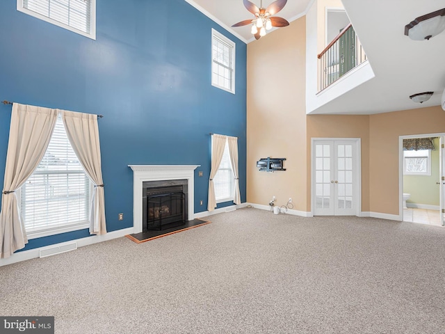 unfurnished living room with carpet floors, visible vents, ornamental molding, french doors, and a glass covered fireplace