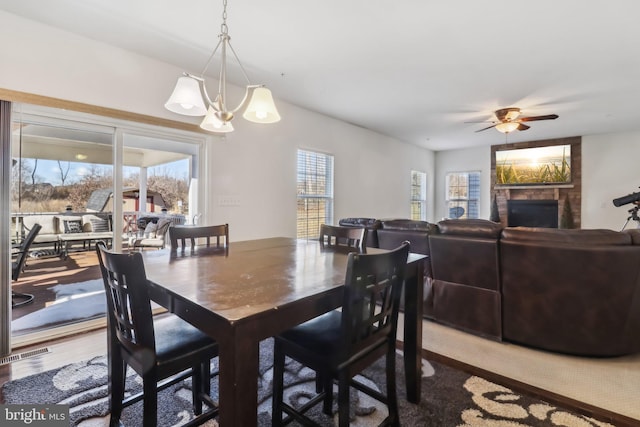 dining space featuring hardwood / wood-style flooring, a fireplace, ceiling fan with notable chandelier, and a wealth of natural light