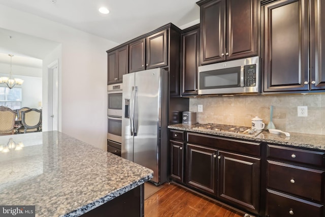 kitchen with stainless steel appliances, tasteful backsplash, dark wood-type flooring, and a notable chandelier