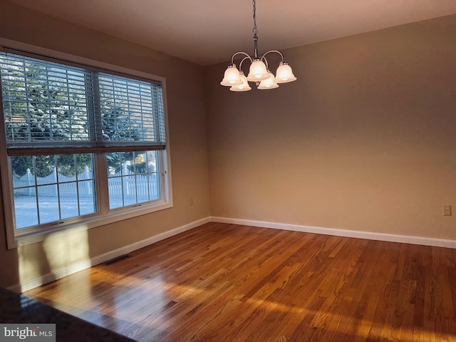 empty room featuring wood-type flooring and a notable chandelier