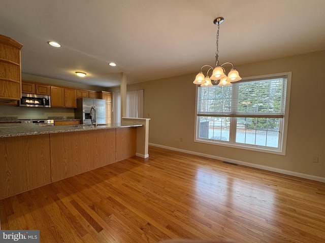 kitchen with decorative light fixtures, a chandelier, kitchen peninsula, stainless steel appliances, and light hardwood / wood-style floors