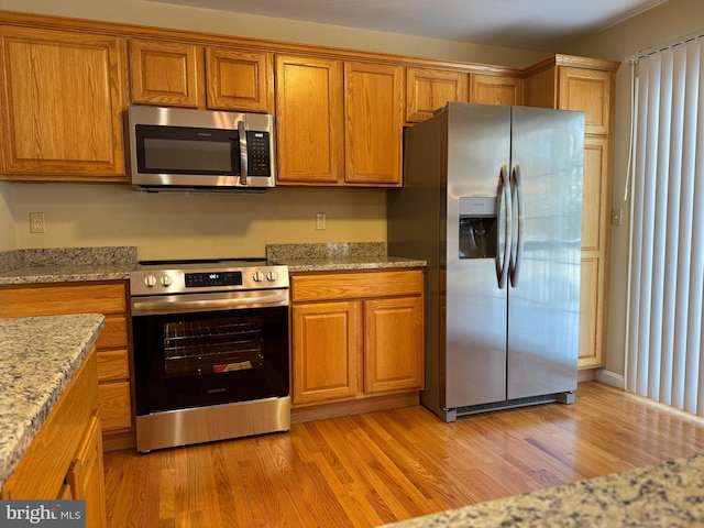 kitchen featuring stainless steel appliances, light stone counters, and light hardwood / wood-style floors