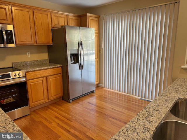 kitchen with light stone counters, light hardwood / wood-style floors, and appliances with stainless steel finishes