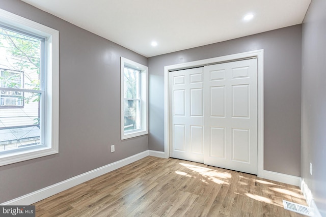 unfurnished bedroom featuring a closet, light hardwood / wood-style floors, and multiple windows