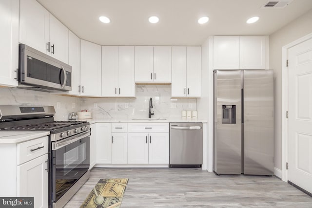 kitchen with stainless steel appliances, sink, light hardwood / wood-style flooring, and white cabinets