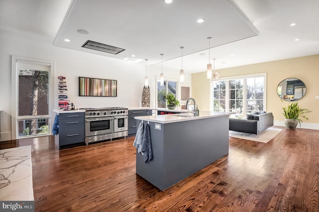 kitchen featuring dark hardwood / wood-style floors, pendant lighting, an island with sink, sink, and double oven range